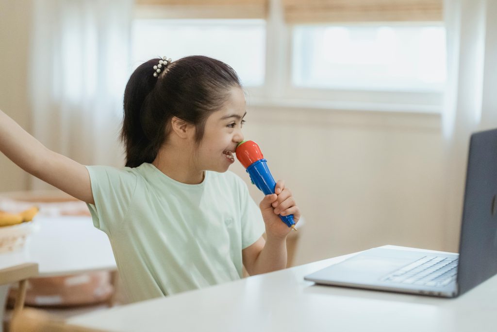 Young girl with Down syndrome holding a toy microphone and looking at a laptop